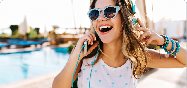 giovane donna con berretto rosso e cappotto beige cammina felicemente per una strada cittadina. Sullo sfondo si intravede un edificio storico con cupola. Elementi grafici circolari blu e turchesi decorano l'immagine.