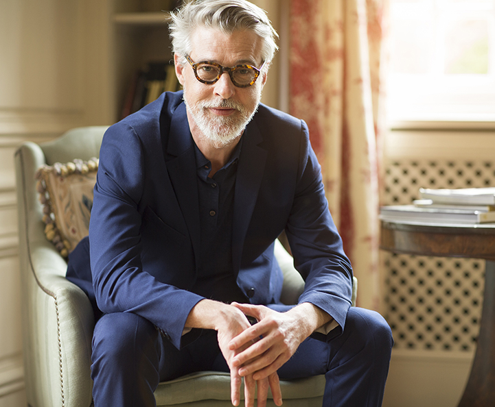 donna bionda sorridente seduta a una scrivania con laptop, tiene in mano una carta di credito blu Nexi. L'ambiente è domestico e luminoso con scaffali bianchi sullo sfondo. Un elemento grafico blu e turchese sovrapposto suggerisce l'e-commerce.